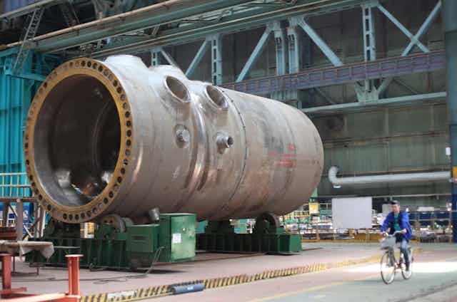 A massive metal cylinder lies on its side in a high-ceilinged factory.