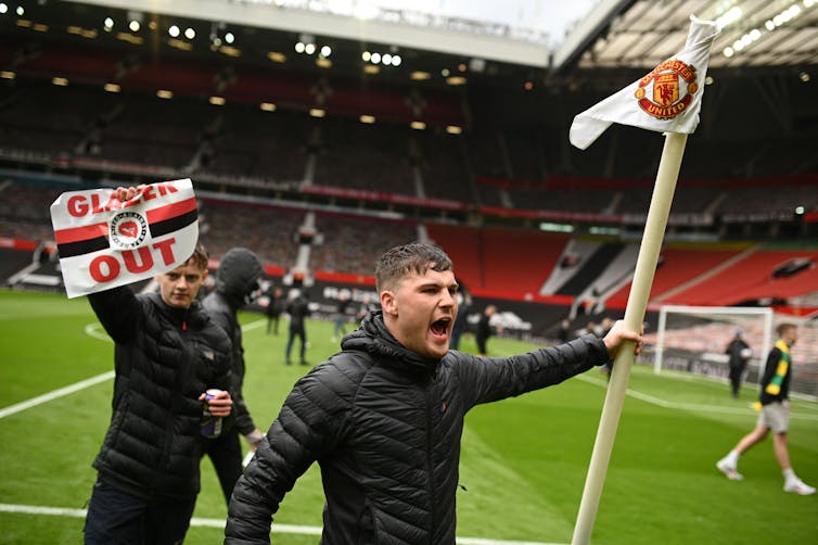 A supporter holds aloft a corner flag while another holds a sign saying 'Glazer out.'