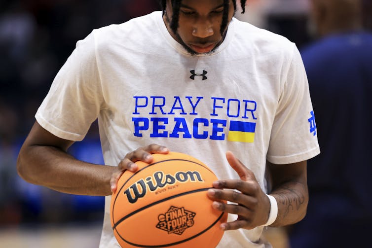 A man holds a basketball wearing a t-shirt that reads 'pray for peace'