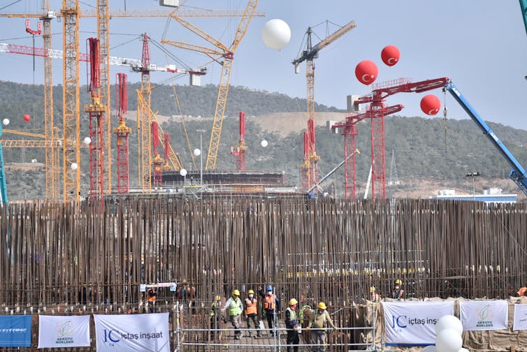 Cranes decorated with balloons loom behind a fence at a construction site.