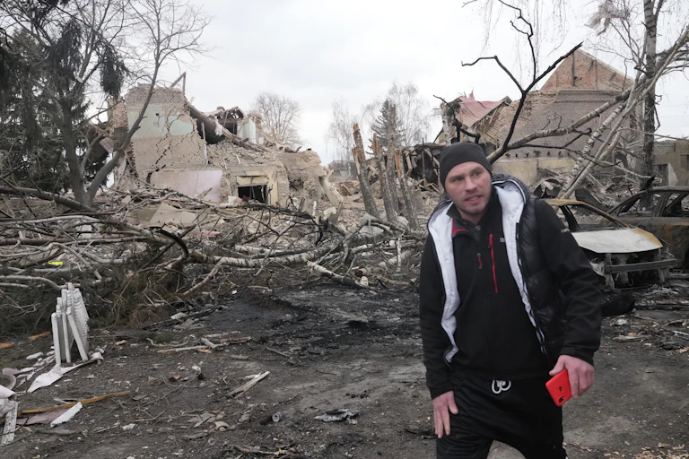A man walks past rubble and burned out cars.