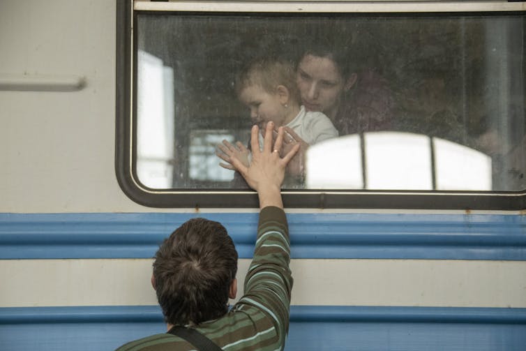 Woman and small child on train say goodbye to man.