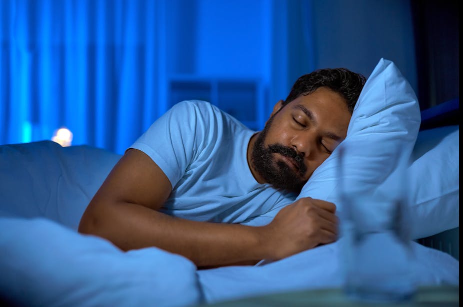 An adult man sleeps in bed on his side with his head resting on a pillow.