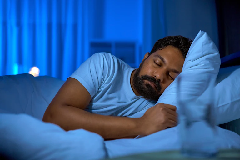 An adult man sleeps in bed on his side with his head resting on a pillow.