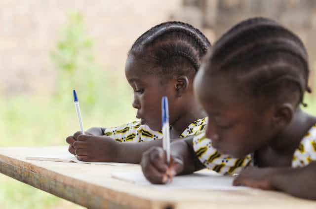 A close-up of two school girls writing in their work books.