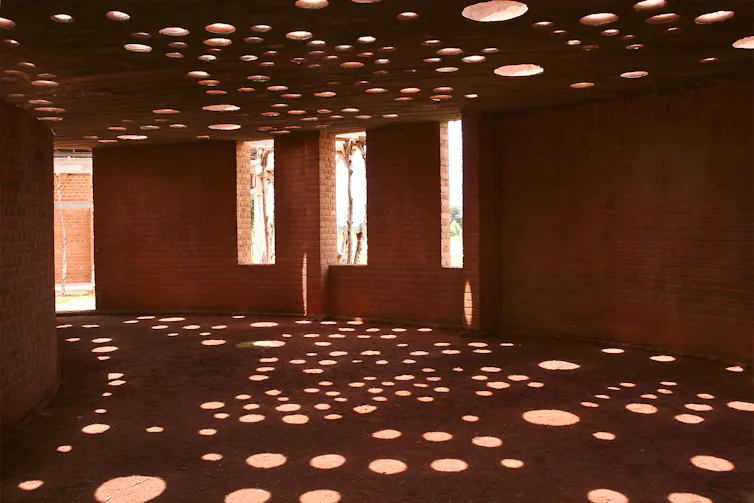 An interior shot of a clay brick building with circular holes in the ceiling, through which light filters down onto the floor