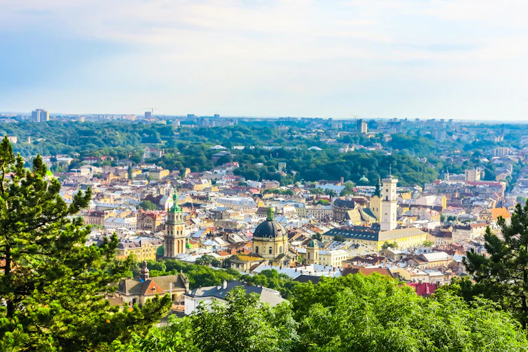 A bird's eye view of an historic city centre with green domed roofs and lots of trees.