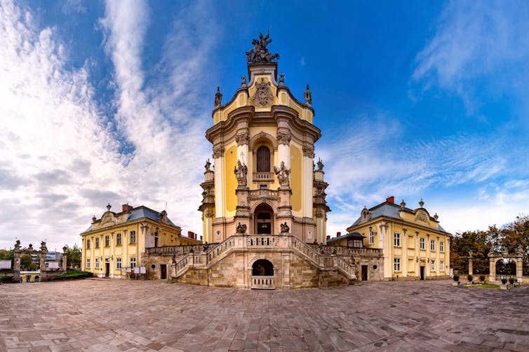 A panoramic view of a roccoco cathedral and plaza, under a blue sky.