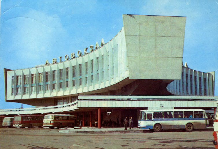 A brutalist concrete curved building with 1980s buses.
