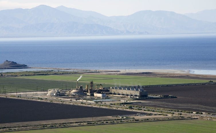 Una central eléctrica rodeada de campos con un gran lago detrás y montañas en la distancia.