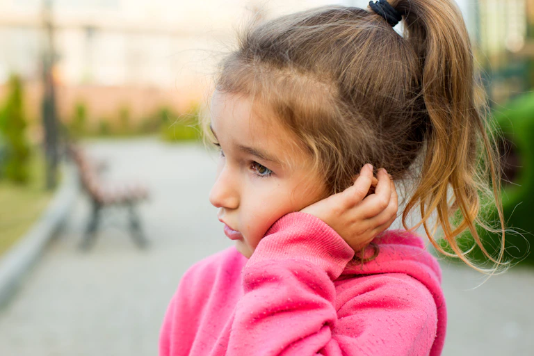 little girl in pink sweater holding her cheek due to tooth pain