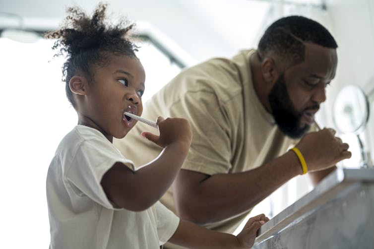 Little girl and dad brushing their teeth together.