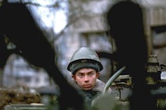 A soldier's face is seen between two black columns.