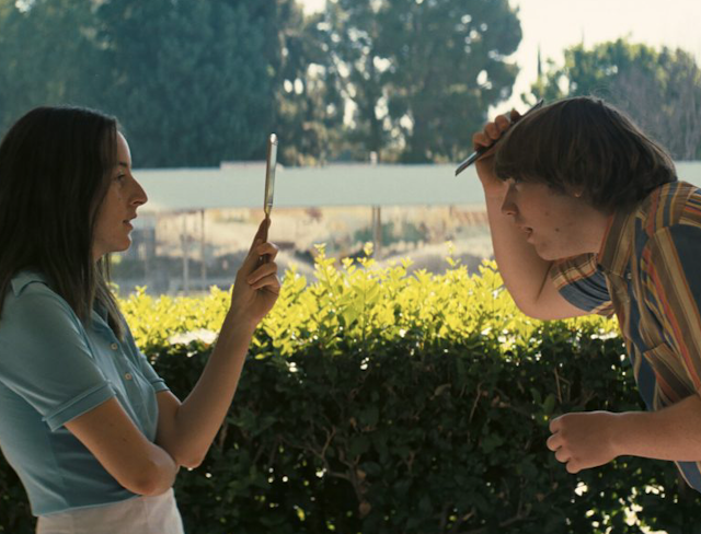 Girl holds up mirror in front of boy combing his hair.