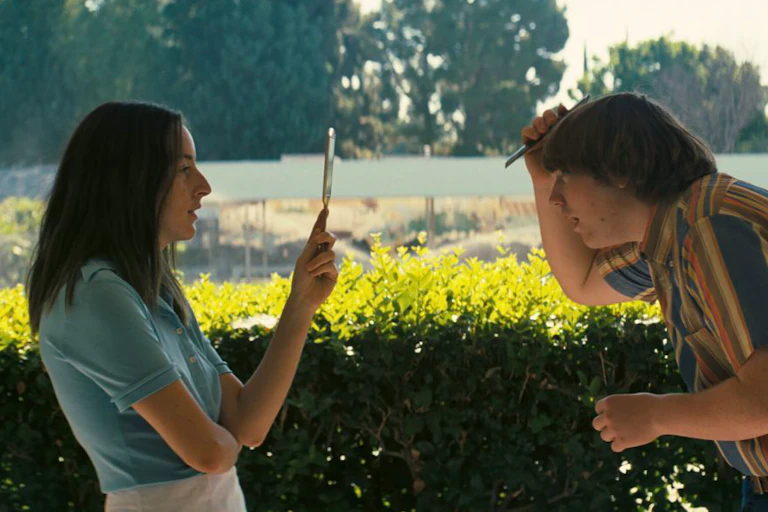 Girl holds up mirror in front of boy combing his hair.