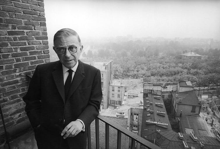 Man stands on balcony holding a cigarette.