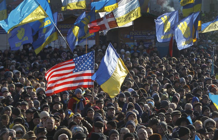 Protestors many holding Ukrainian, American and other flags gather in a square in Kyiv