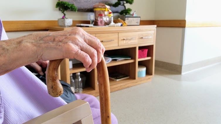 Aged care resident holds a cane while sitting in their room.
