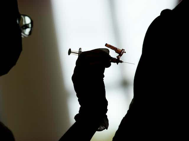 Silhouette of a gloved hand about to inject an arm with a syringe