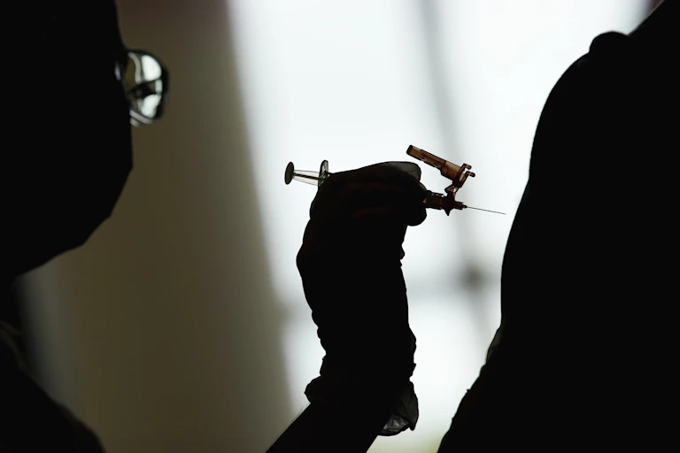 Silhouette of a gloved hand about to inject an arm with a syringe