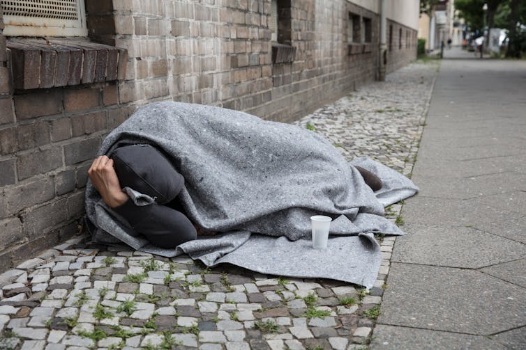 A homeless man, covered by a blanket, sleeping on the street