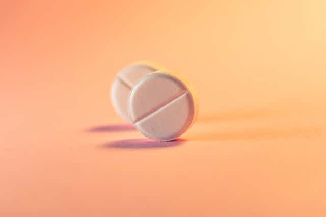 Two round white pills against a light orange background.