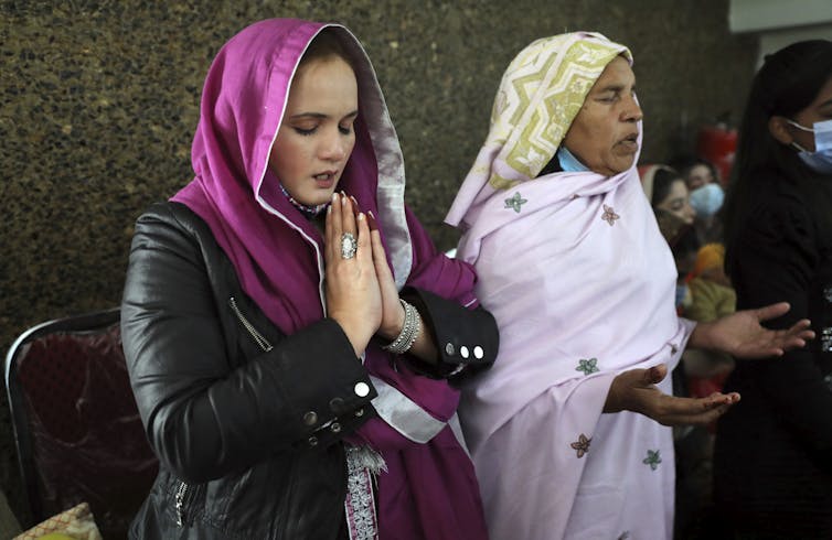 Two women wearing head coverings pray inside a church.