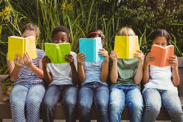 Five children sit in a row reading from brightly coloured books