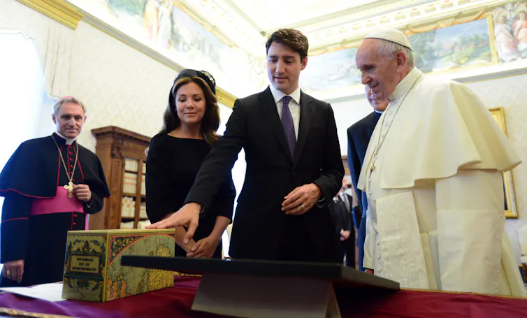 A man in a suit is seen pointing to a table and a set of books.