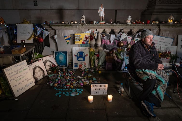 Richard Ratcliffe sitting on a camping chair outside a government building in front of candles and photos of his wife Nazanin Zaghari-Ratcliffe.