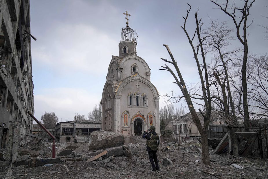 A soldier stands in front of a church surrounded by debris from shelling.