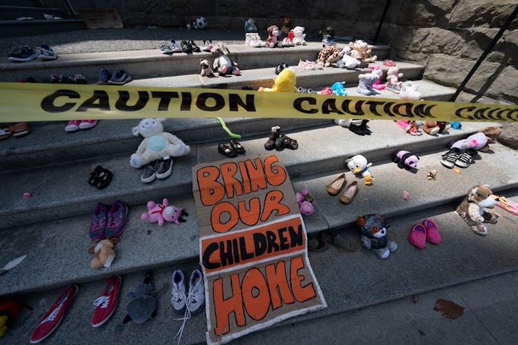 Children's shoes seen on church steps with the sign 'Bring our children home.'