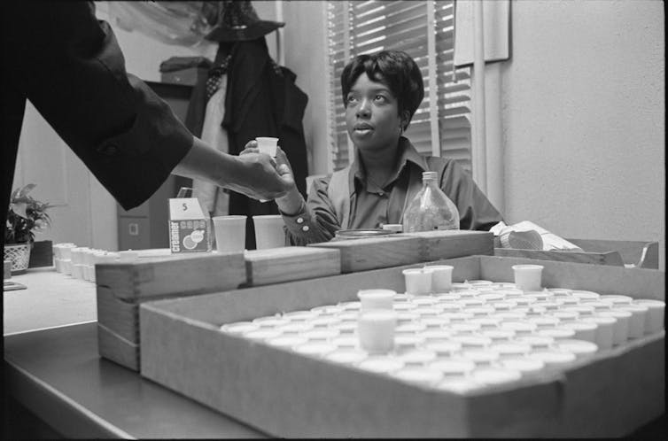 A nurse hands a cup to a woman in a black and white photo.