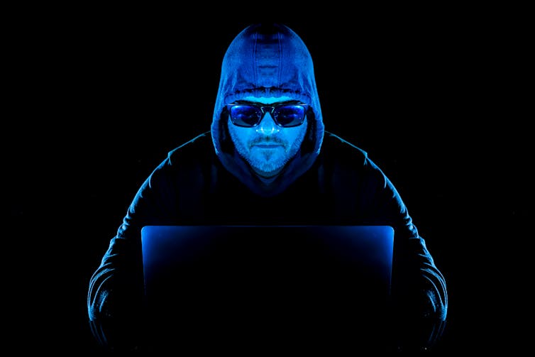 a man wearing a hooded sweatshirt and sunglasses types on a laptop computer