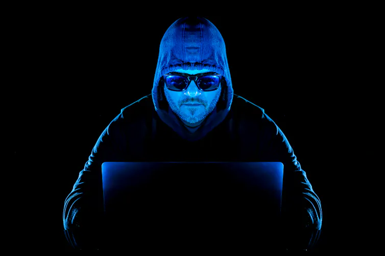 a man wearing a hooded sweatshirt and sunglasses types on a laptop computer