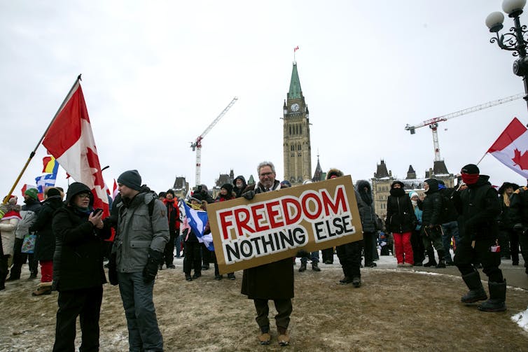 A man stands in front of a crowd holding a sign that says 'FREEDOM NOTHING ELSE'