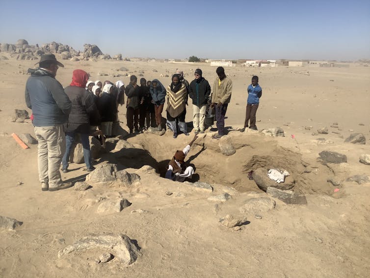 people cluster around a pit in an arid landscape