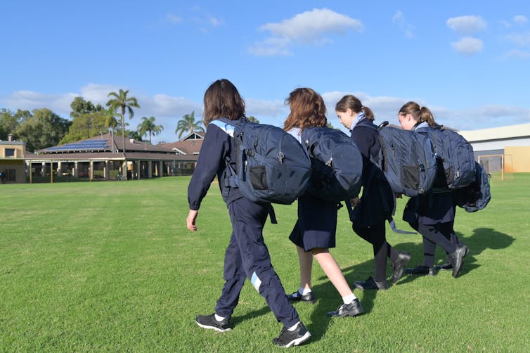 High school students wearing backpacks are walking in a group on an oval.