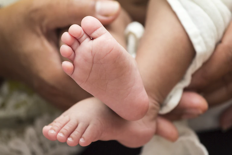 First Nations Mum hold's baby's legs, showing the underside of their feet.