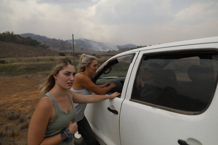 two worried women approach vehicle with smoky sky in background