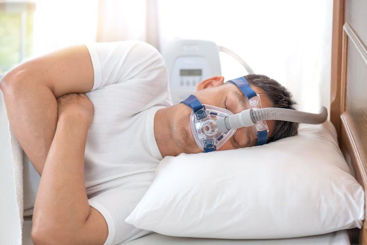 Man in bed with mask on his face and tubes linked to a machine.