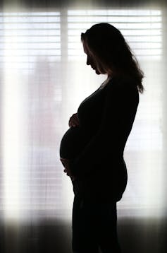 Pregnant woman in silhouette in dark room