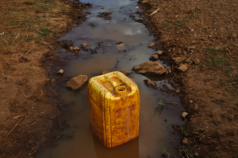A yellow jerrycan sits in a dirty river