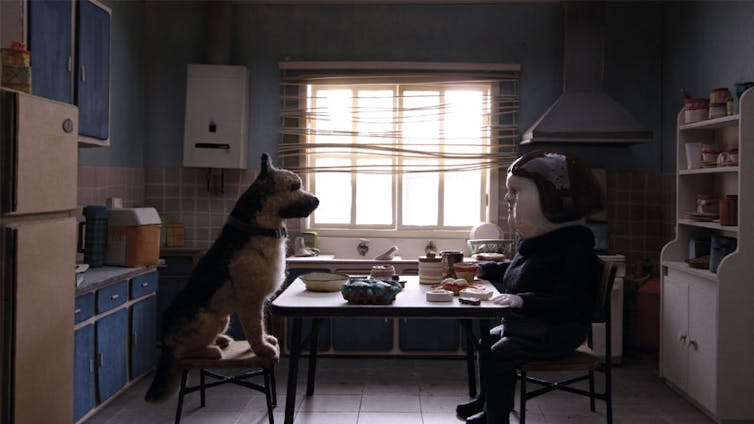 Claymation dog and woman sit at a dining table in a kitchen.