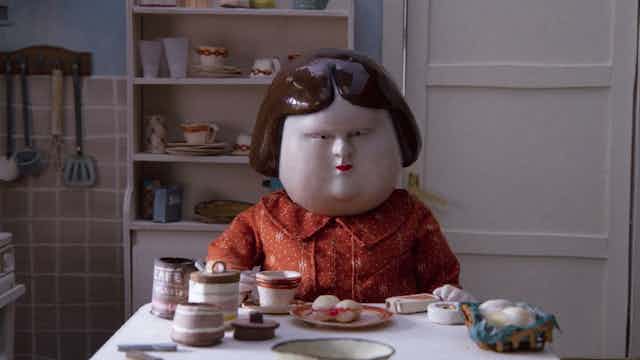 Clay animation of a woman eating at a table.