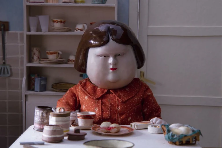 Clay animation of a woman eating at a table.