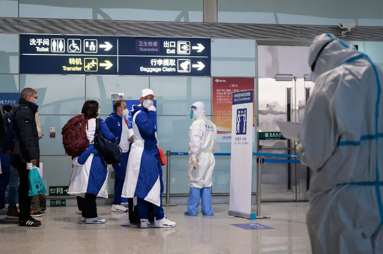 Groupe de sportifs protégés par des masques et des tabliers attendant devant des responsables chinois en combinaison