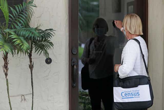 A person holding a shoulder bag reading "United States Census Bureau" knocks on a door.