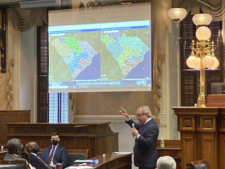 A man gestures to a screen showing two maps of South Carolina's political districts