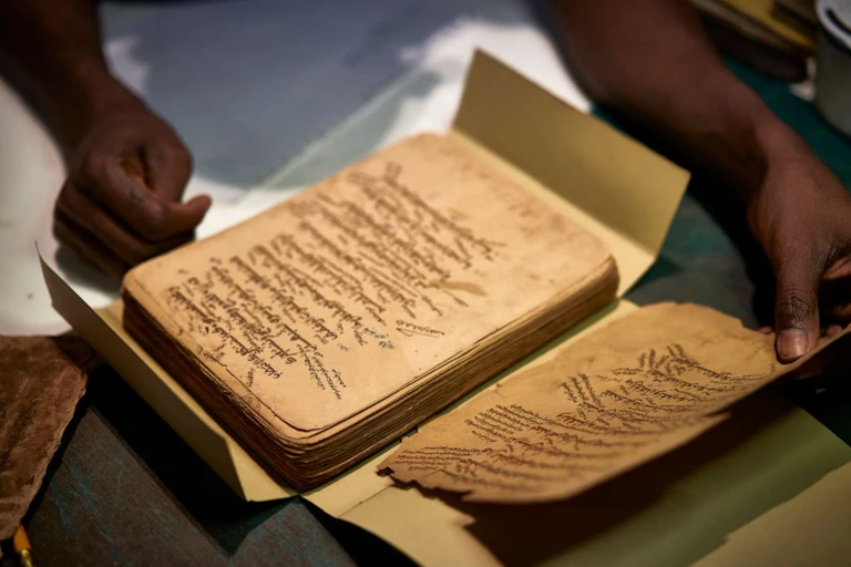 two hands hold a pile of ancient-looking papers on a person's lap.